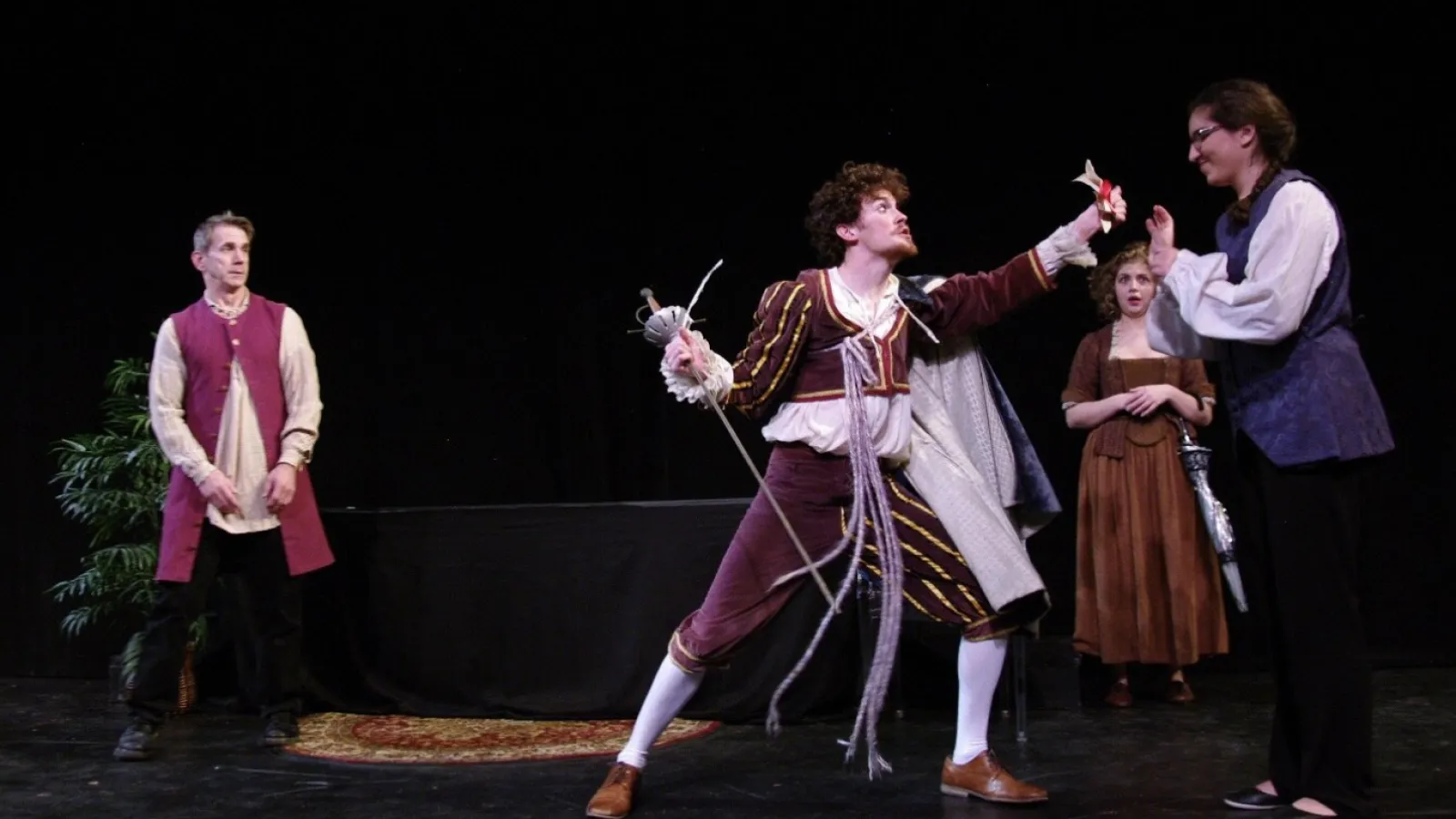 Four actors on a stage wearing Shakespearean era clothing